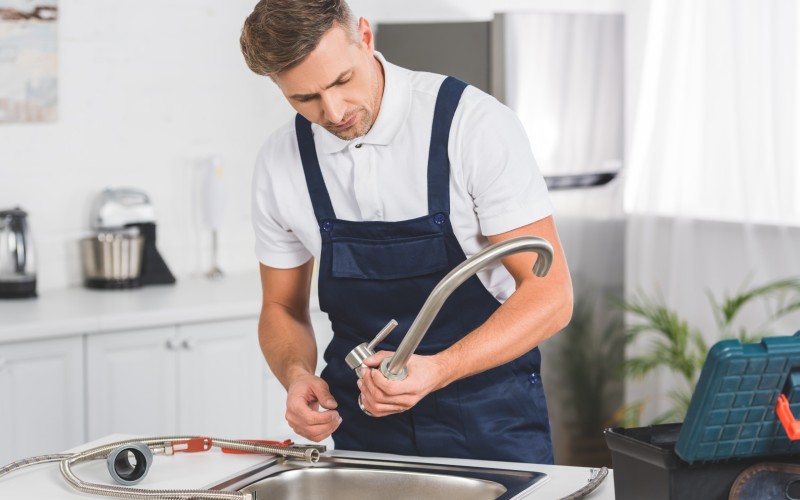 thoughtful adult repairman taking off kitchen faucet for repairing